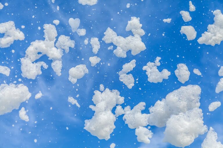 Clumps of lightweight white party foam suds floating through the air against a vibrant blue sky.
